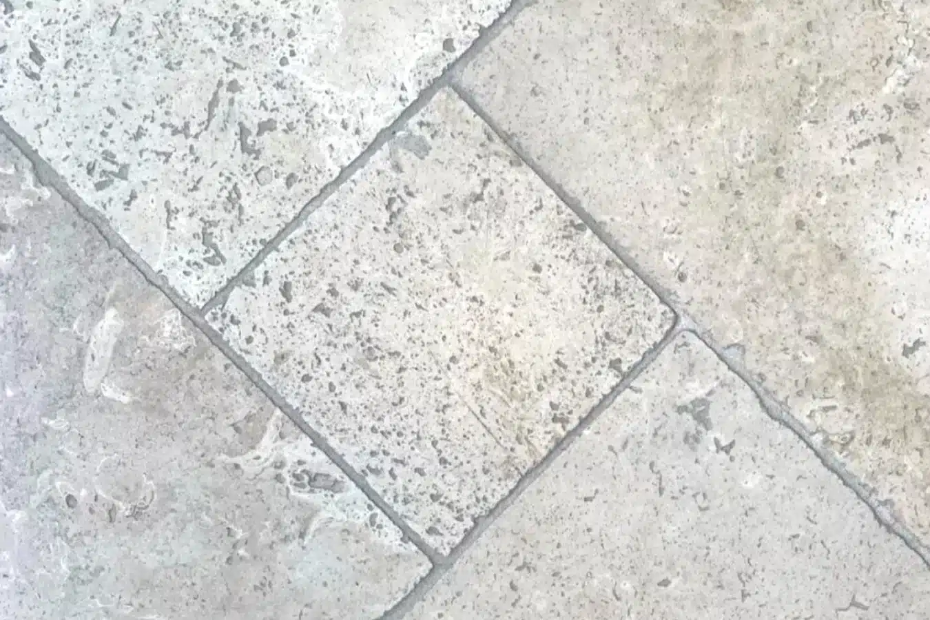 Sol intérieur en dalles de travertin Mix posées en opus, surface ternie et grisée avec des traces sombres dans les pores et les joints